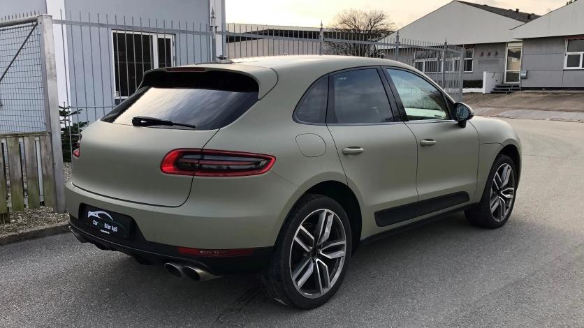 En grøn SUV parkeret ved en bygning med metalhegn i baggrunden.