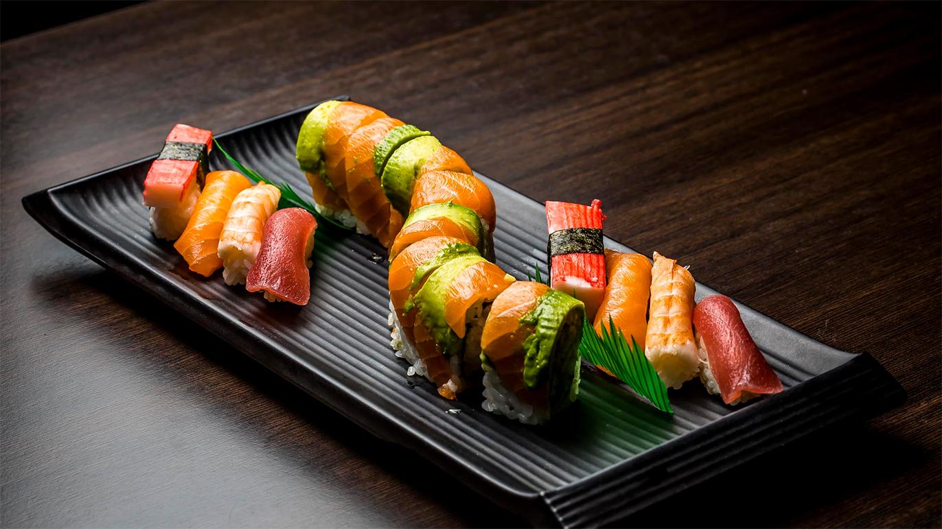 Farverig sushi anrettet på en sort tallerken med forskellige typer nigiri og maki.