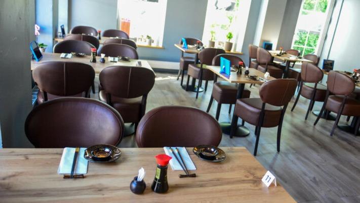 Indendørs restaurant med brune stole, træborde og dækkede borde klar til gæster.