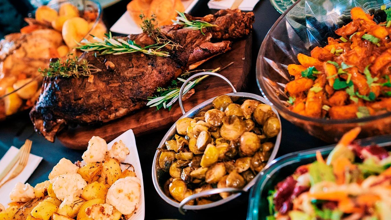 Et festligt bord med lækker mad, herunder stegt lam, grøntsager, kartofler og salat.