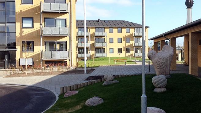 Moderne bygninger med balkoner og en gårdhave med skulpturer og grønne områder.