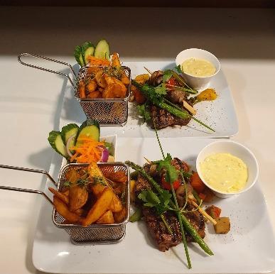 To retter med grillet kød, pomfritter i kurve, friske grøntsager og en skål med sauce på en hvid tallerken.