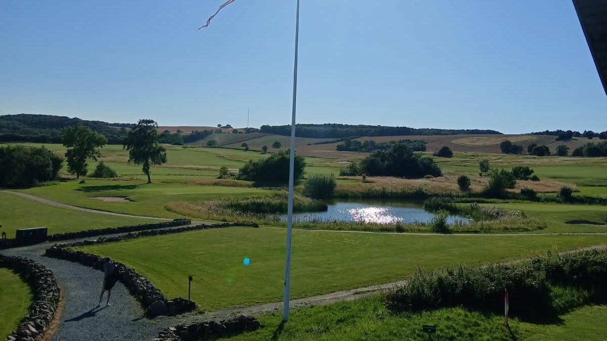 En smuk udsigt over en grøn golfbane med en sø og træer under en klar blå himmel.