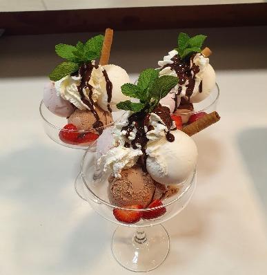 Tre is-sundae med chokolade, flødeskum, friske jordbær og mynte i glas.