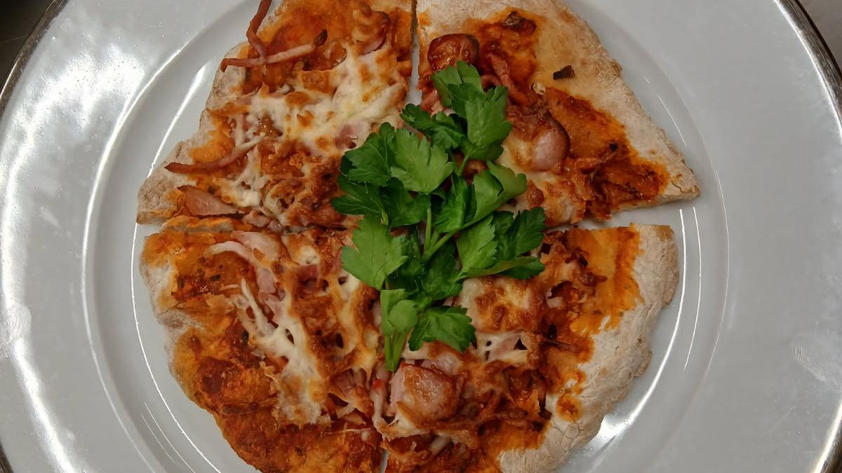 En pizza med kylling, ost og koriander på en hvid tallerken.