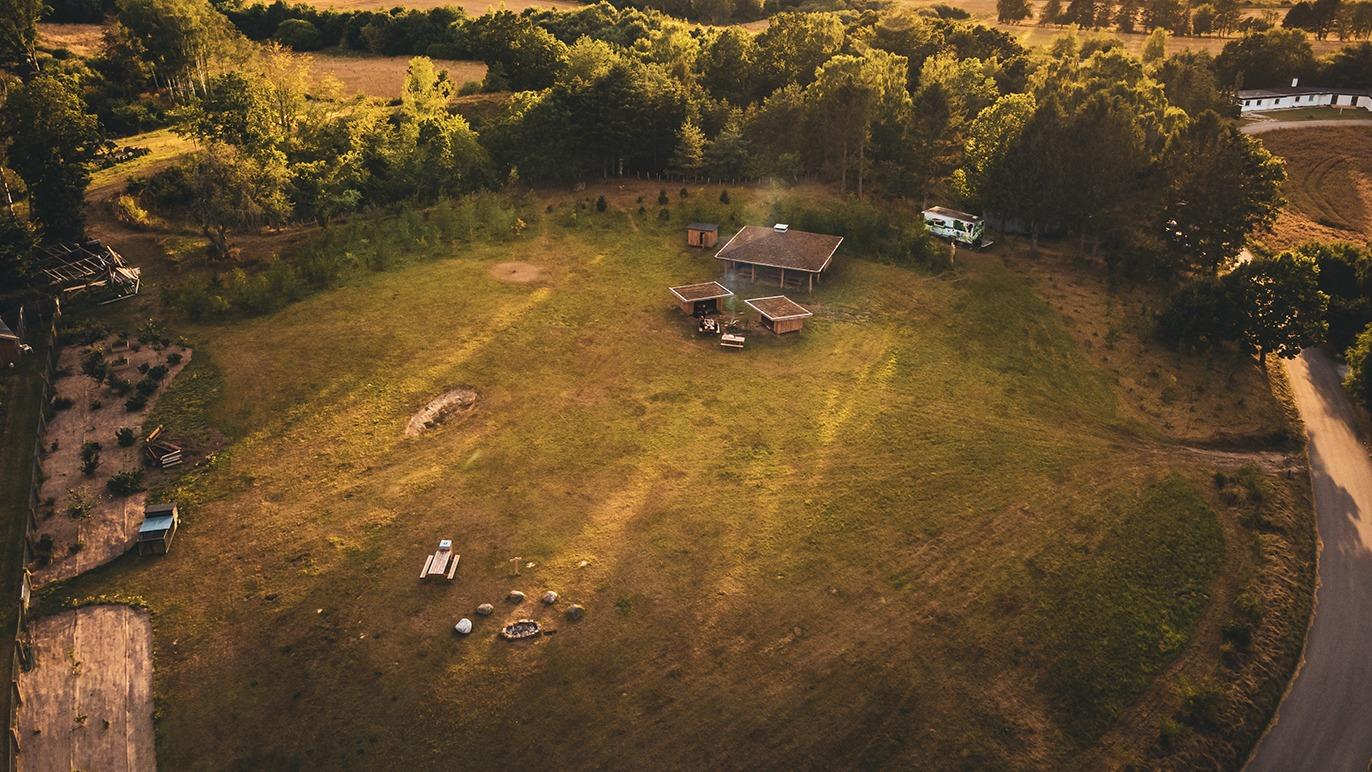 En luftfoto af en stor græsplæne med et hus og træer i baggrunden, beliggende i et landligt område.