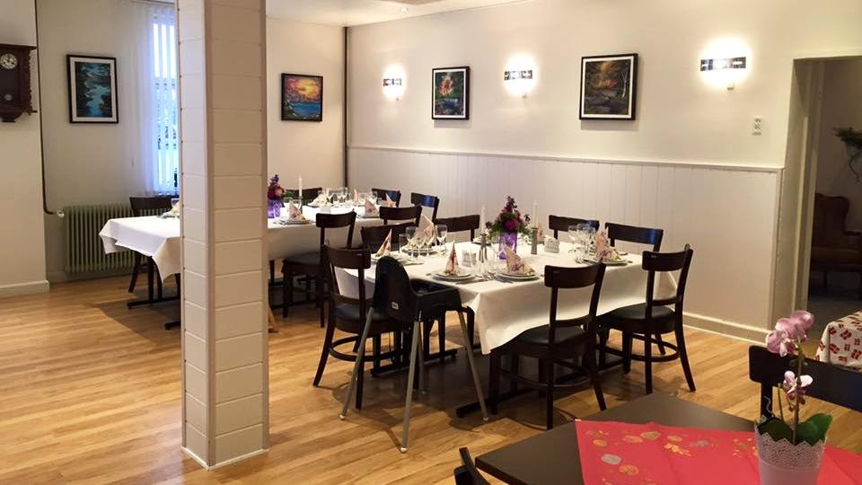 En hyggelig restaurant med dækkede borde, stole og kunstværker på væggene. Trægulv og blødt lys skaber en indbydende atmosfære.