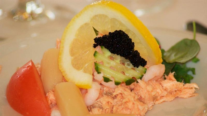 Lækker ret med laks, rejer, agurk, caviar og citronskive på en tallerken.