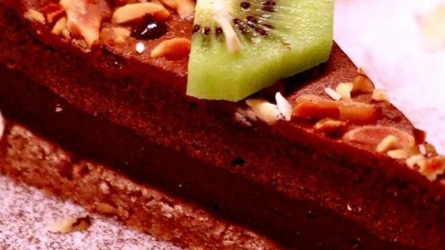 Lækkert stykke chokoladekage med nødder og en skive kiwi på toppen.