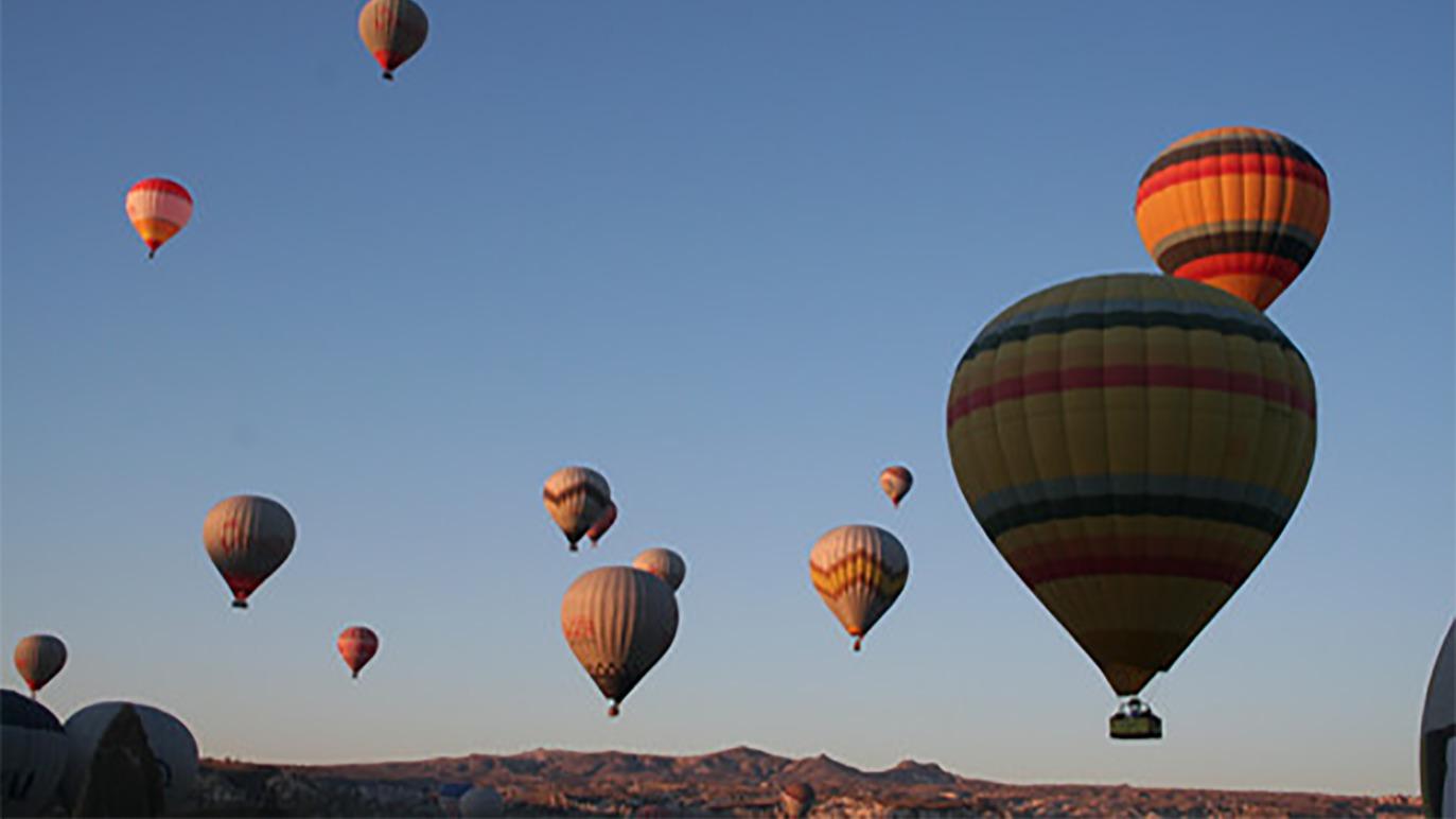 Farverige luftballoner svæver over landskabet ved solopgang i en klar himmel.