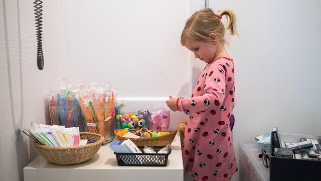 Pige i rosa pyjamas står ved et bord med farverigt håndarbejdsmateriale og kigger på en kasse med perler.
