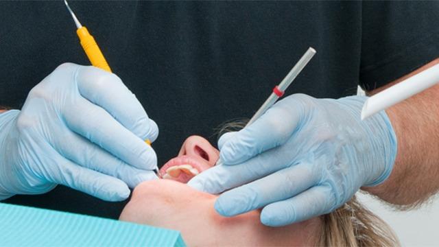 En tandlæge udfører en tandbehandling på en patient med handsker og værktøj.