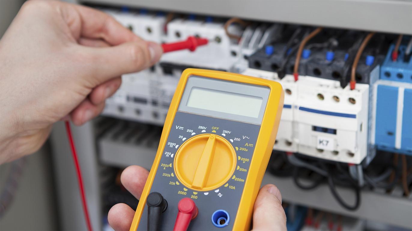 En person bruger et multimeter til at måle elektrisk spænding i en elektrisk tavle.