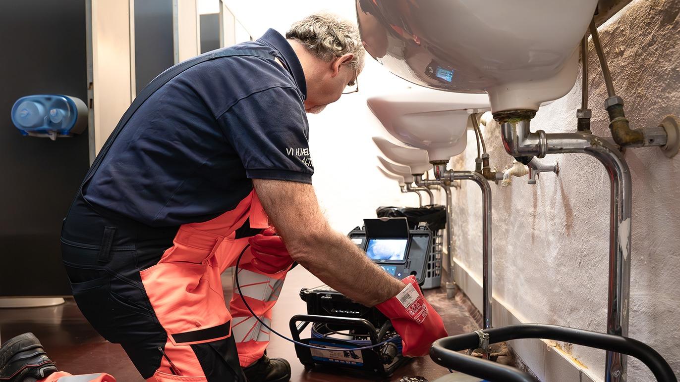 En håndværker arbejder på rør under håndvaske i et toilet, mens han bruger værktøj og udstyr.