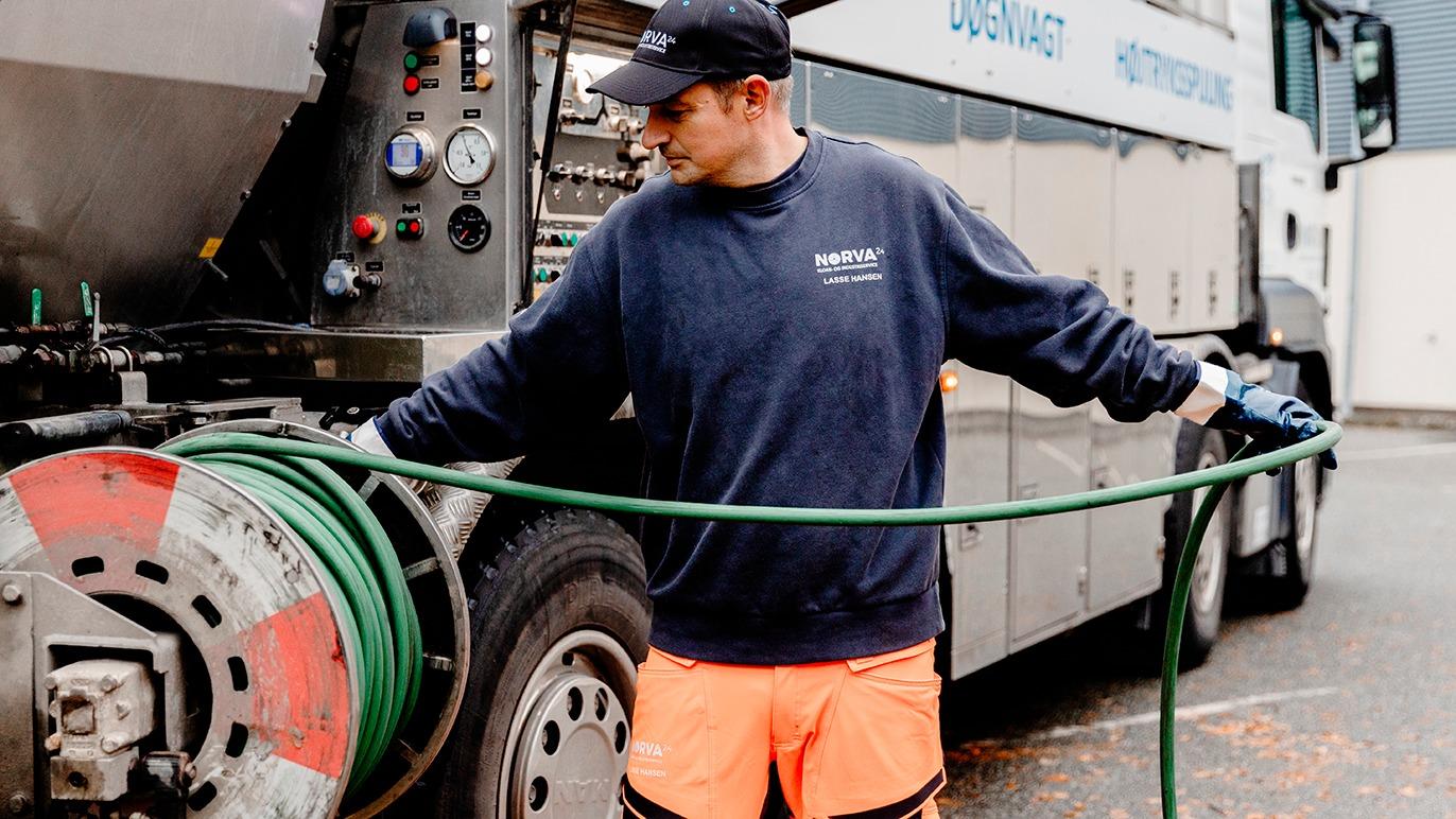 En mand i arbejdstøj trækker en slange fra en lastbil med udstyr til rensning.