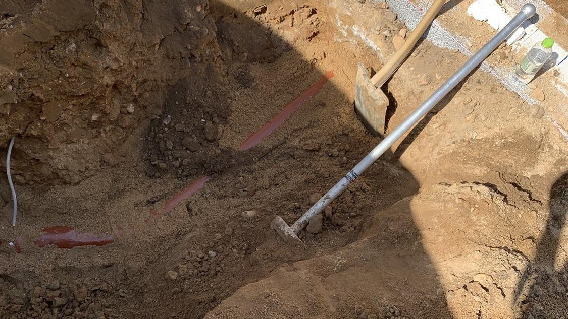Gravested med en skovl og rør synlige i jorden, klar til byggearbejde eller installation.
