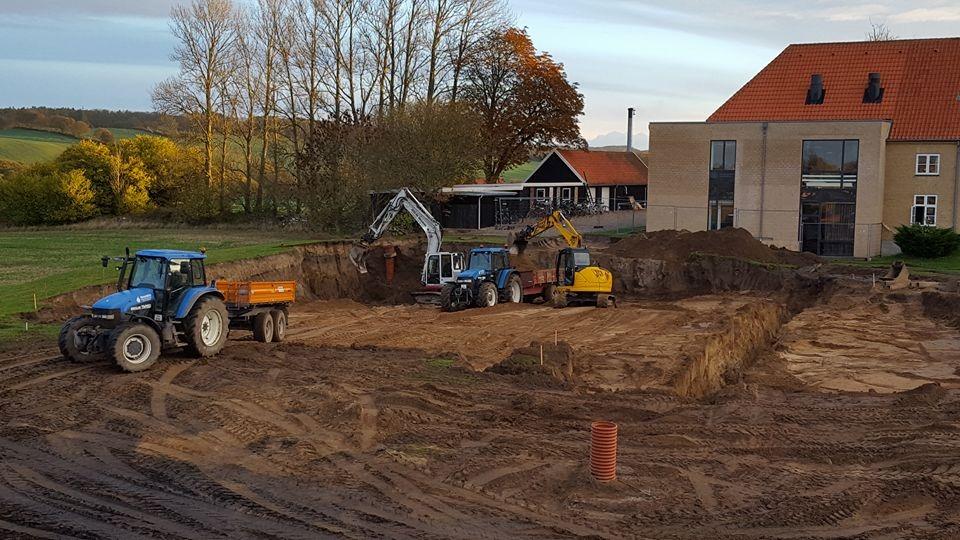 Byggeplads med gravemaskiner og traktorer, der arbejder på at forberede jorden til et nyt byggeri.