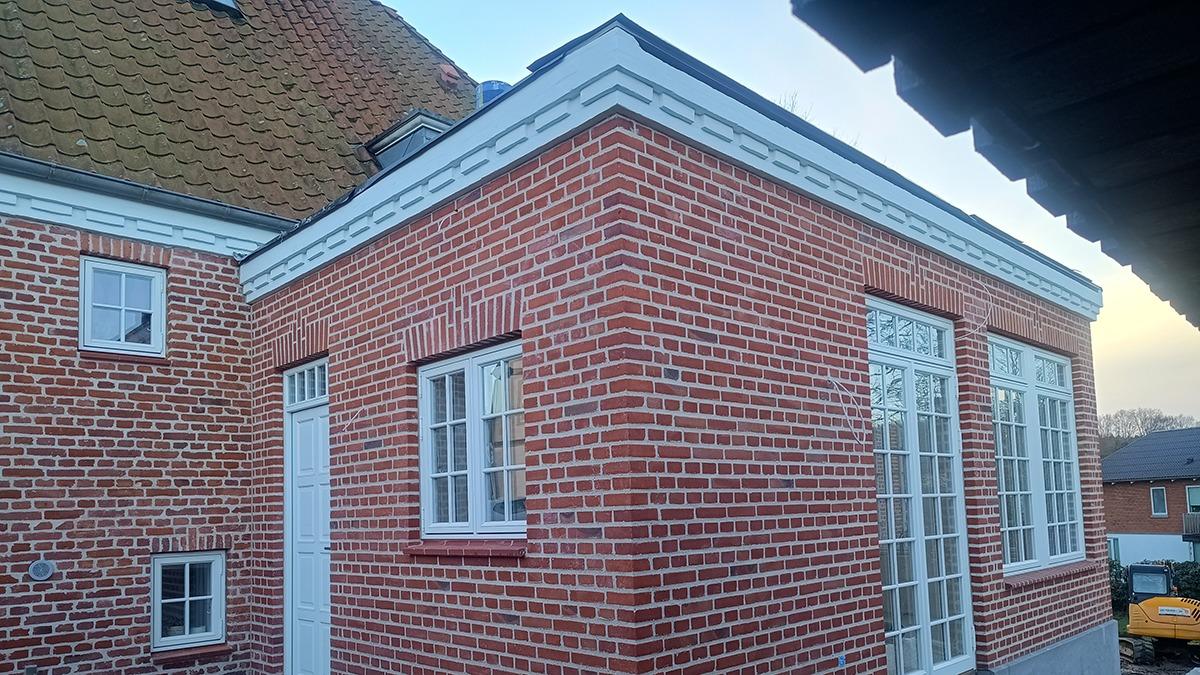 Et murstenshus med store vinduer og en hvid dør, beliggende i en rolig boligområde.