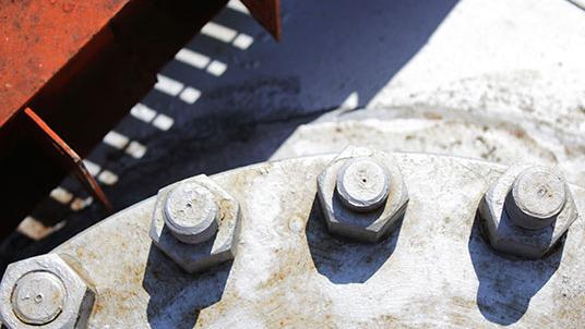 Nærbillede af store bolte og møtrikker på en metaloverflade, der viser slid og rust.