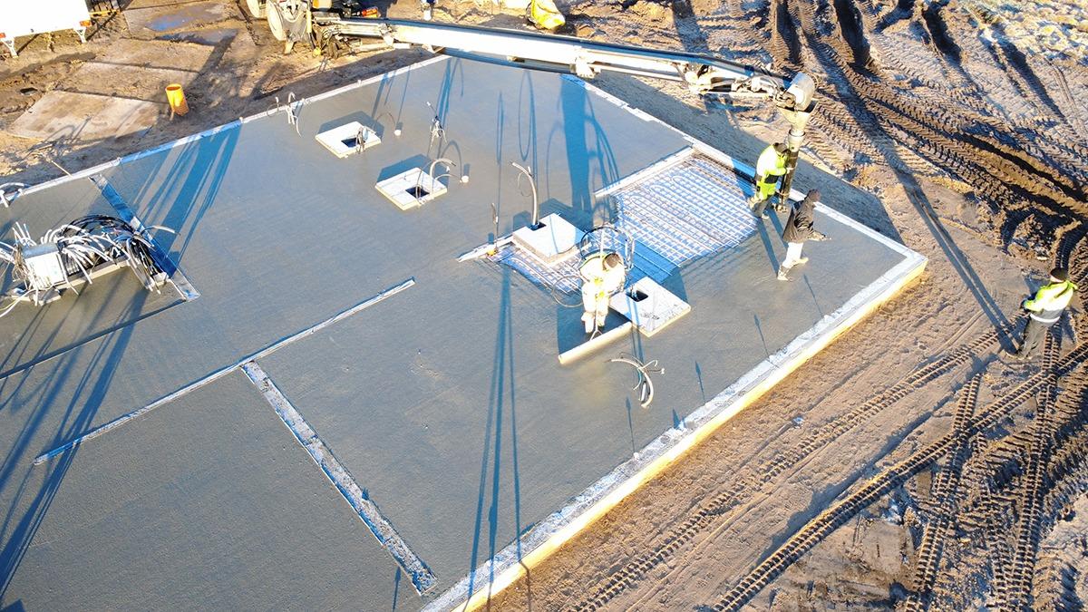 Arbejdsplads med håndværkere, der støber beton på en byggeplads med fundament og afløb.