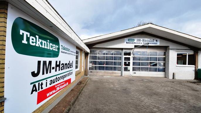 Autoværksted med skilt for JM-Handel, der tilbyder autodele og reparationstjenester.