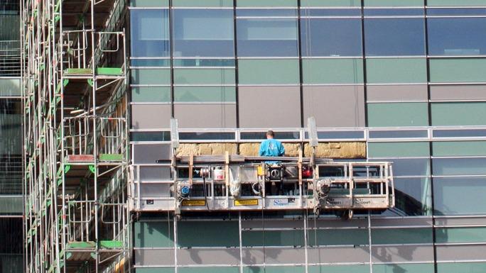En arbejder på en stilladsplatform, der rengør vinduerne på en moderne kontorbygning.