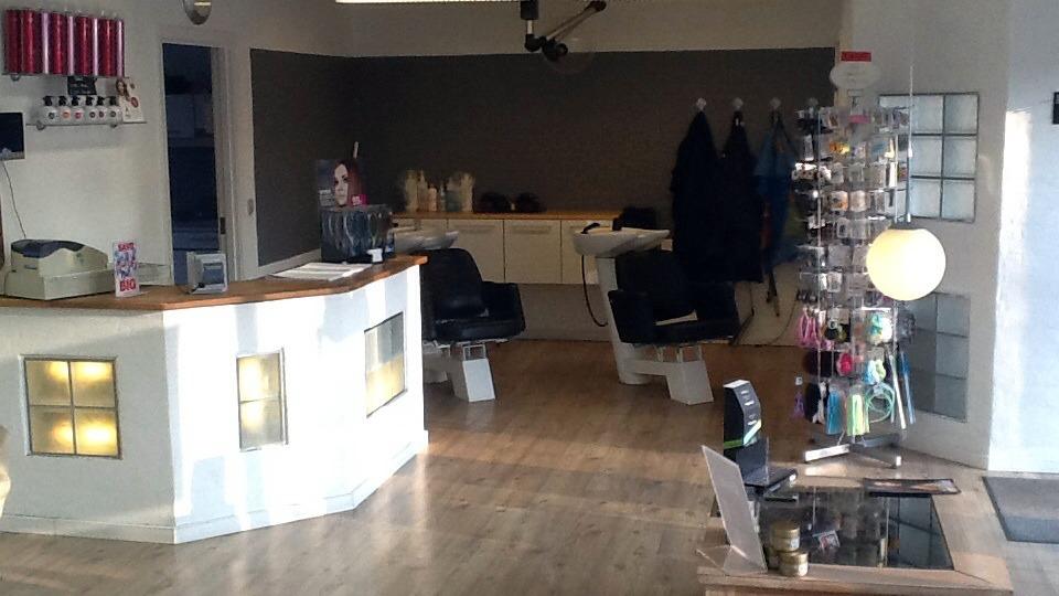 Frisørsalon med moderne indretning, herre- og dameklippestole samt en reception med en lys lampe.