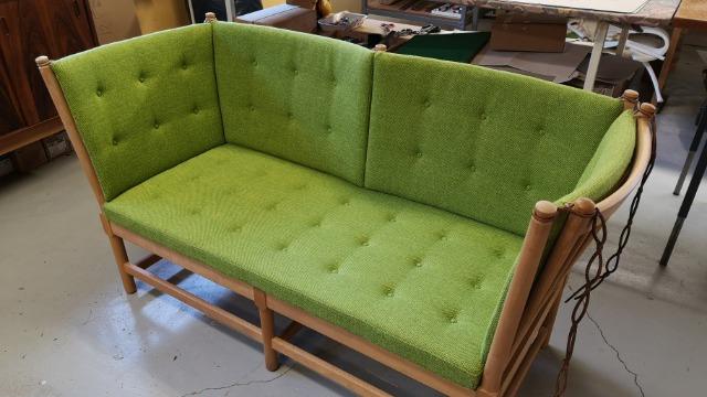 En grøn sofa med tuftede puder og træramme, placeret på et gulv i et værksted.