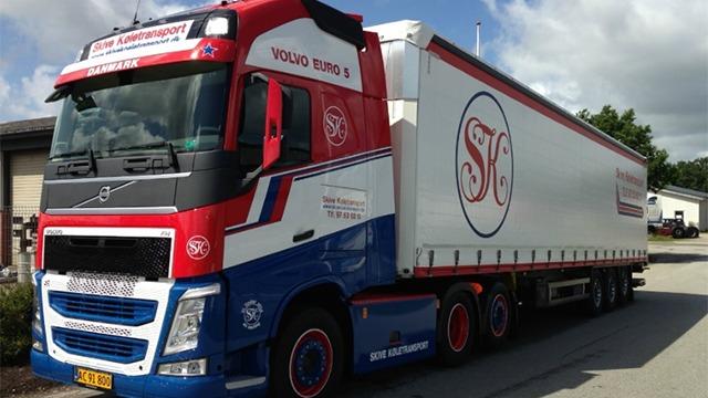 En stor Volvo lastbil med rød, hvid og blå farve, parkeret ved en bygning.