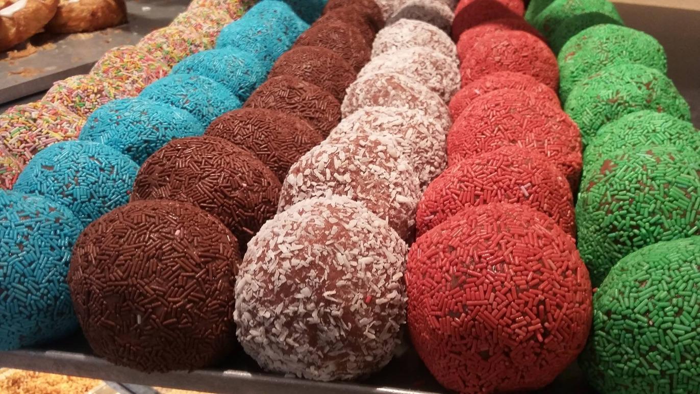 Farverige chokoladebolde dækket med krymmel og kokos, præsenteret i en række på en bageplade.