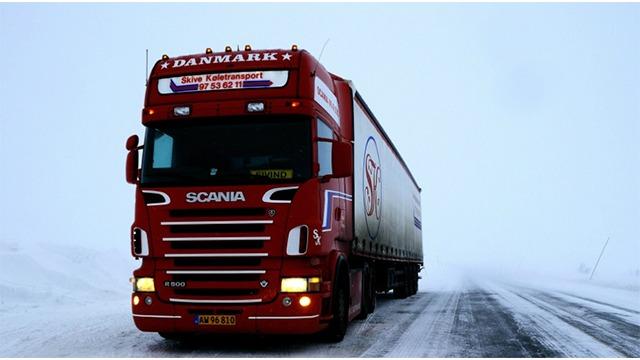 En rød Scania lastbil parkeret på en snedækket vej i Danmark.