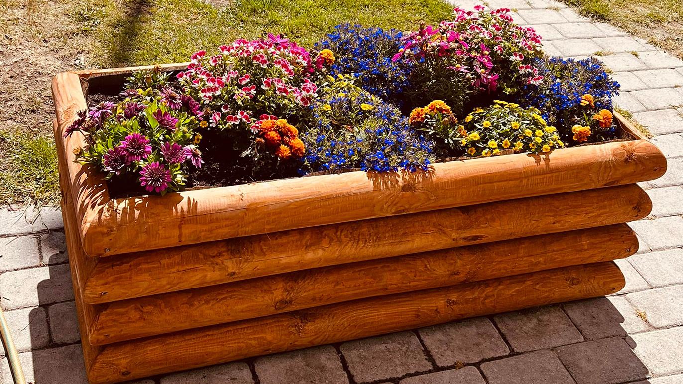 En blomsterkasse i træ fyldt med farverige blomster som petunia og violer, placeret på en stenbelagt terrasse.