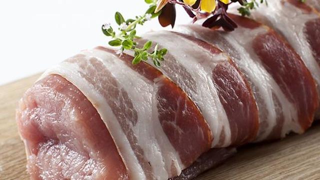 Lækkert stykke kød indpakket i bacon, prydet med friske krydderurter på et skærebræt.