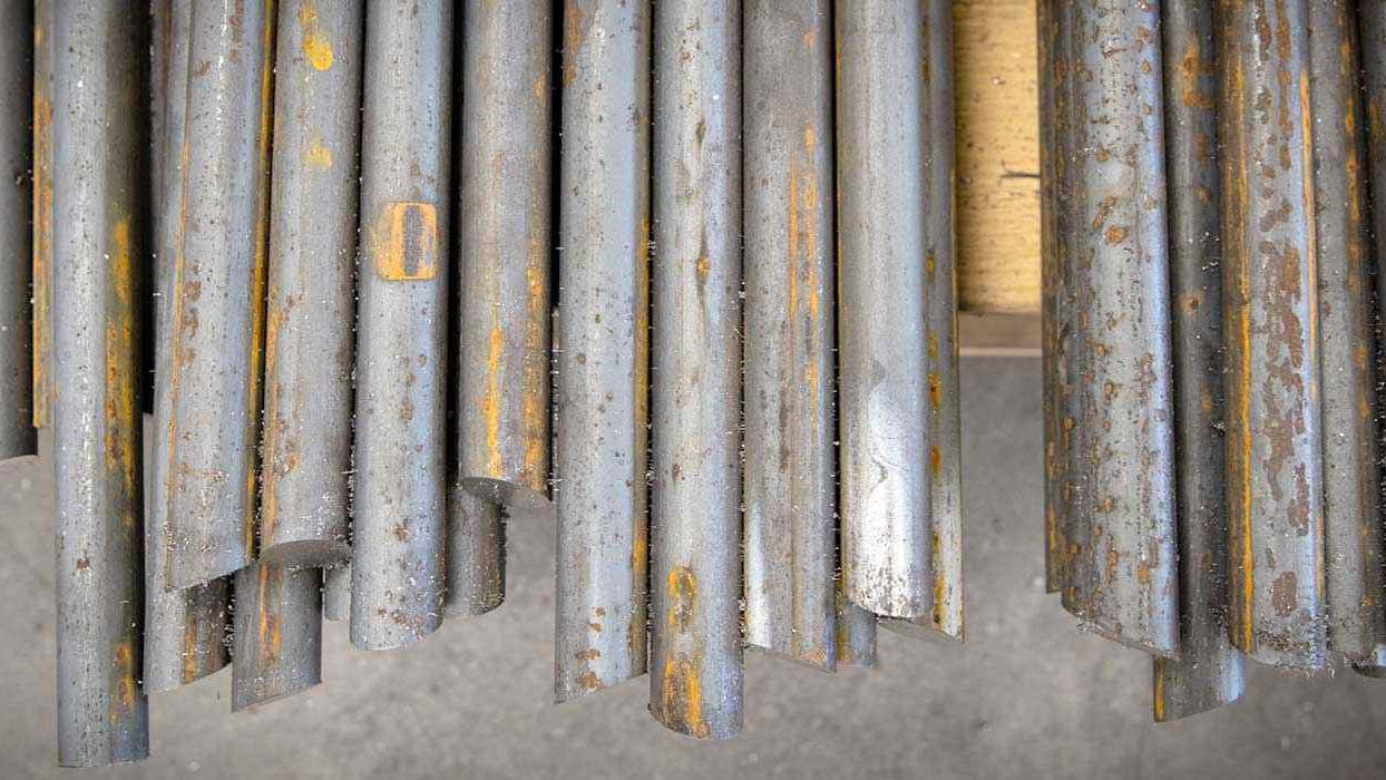 Rustne metalstænger ligger stablet på en betonoverflade i et værksted.