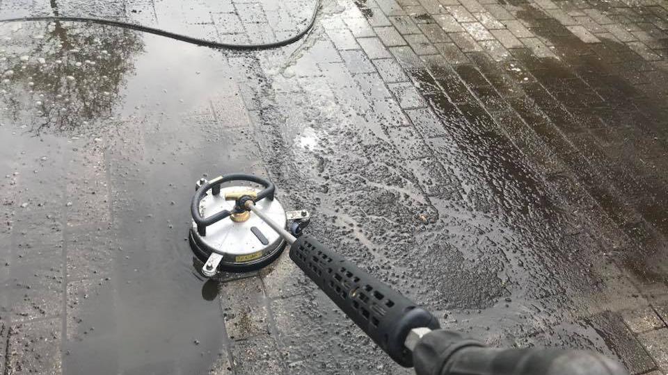 Rengøringsmaskine til fliser, der sprøjter vand på en våd belægning af brosten.