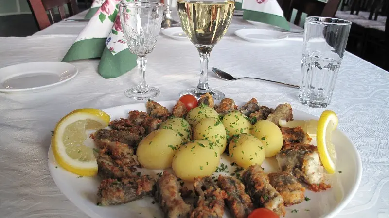 En tallerken med panerede fiskefileter, kartofler, citronbåde og cherrytomater, serveret med hvidvin.