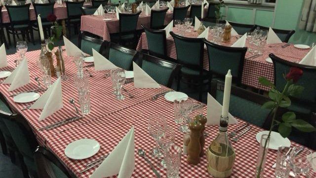 Dækning af et festligt bord med ternet dug, glas, tallerkener og servietter i en restaurant.