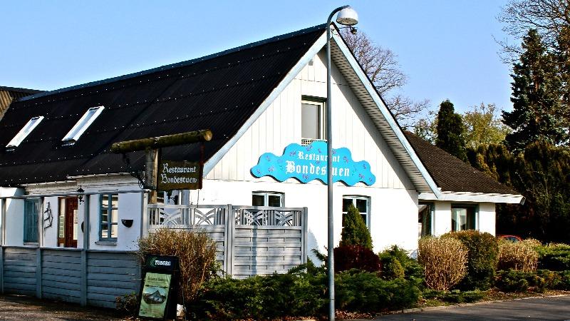 Restaurant Bonbonnière med hvid facade og blå skilt, omgivet af grønne buske og træer.