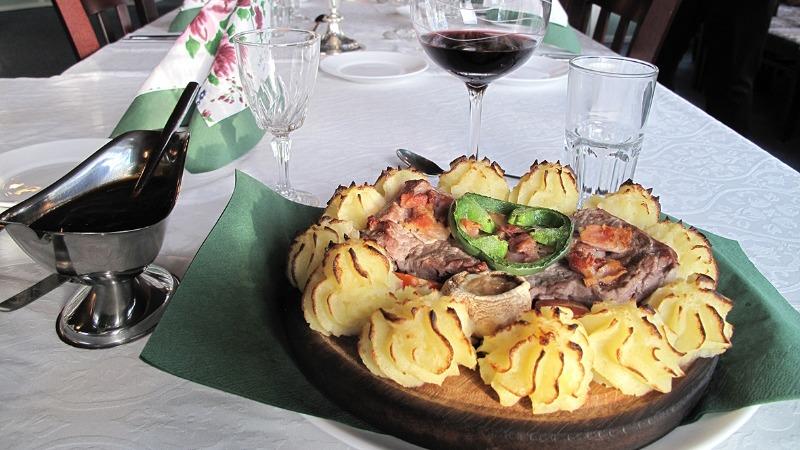 En lækker middag med stegt kød, kartoffelspiraler, grønne grøntsager og rødvin på bordet.