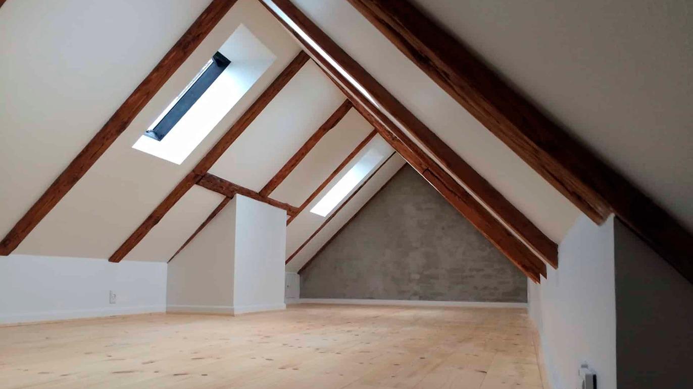 Lyst loft med skrå vægge og synlige træbjælker, der skaber en rummelig atmosfære.