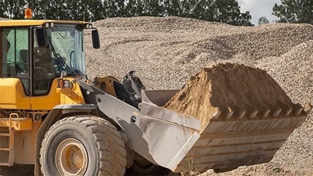 En gummihjulslæsser, der løfter sand fra en stor bunke grus på en byggeplads.