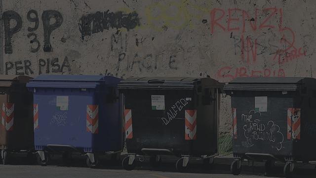 Affaldscontainere i forskellige farver står langs en væg med graffiti.