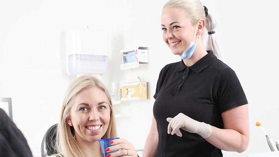 En tandlæge og en patient smiler i en tandklinik, mens patienten holder en tandlægebeholder.