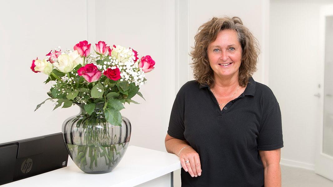 En kvinde står ved en hvid reception med en stor vase med roser og blomster i baggrunden.