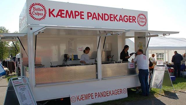 Kæmpe pandekagebod med folk, der bestiller og tilbereder pandekager på en festival.