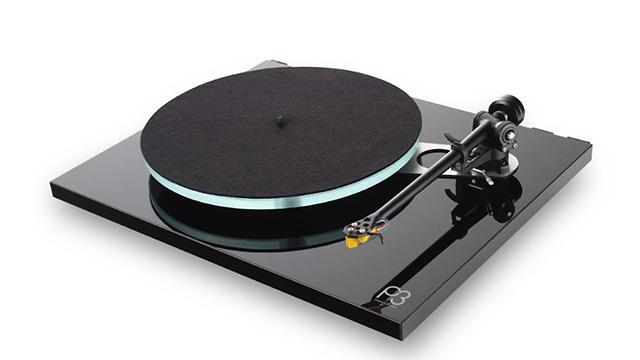 Pladespiller med sort plade og sølvfarvet tonearm på en blank sort base.