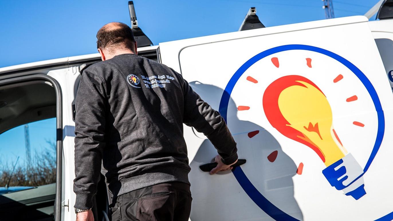 En mand står ved siden af en varevogn med et lysbillede og logo på siden.