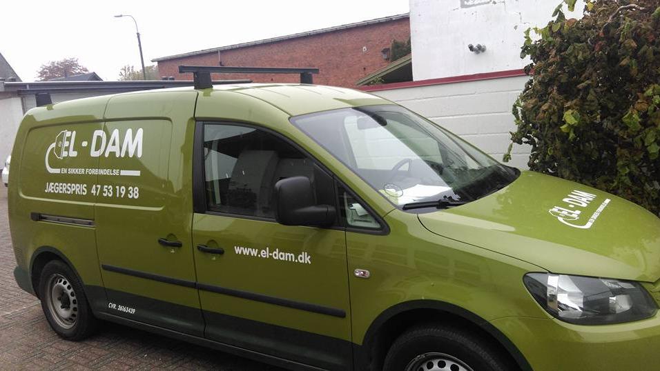 Grøn varevogn med logo og kontaktinformation fra EL-DAM parkeret ved en bygning.