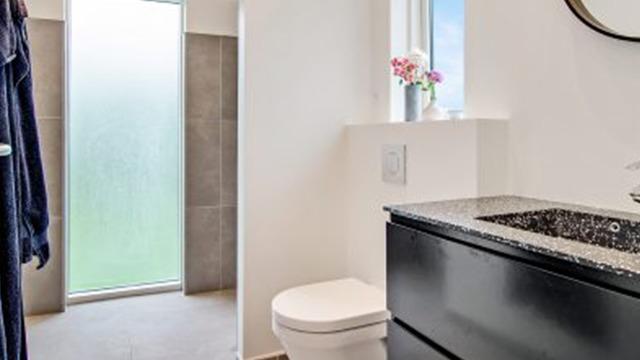 Moderne badeværelse med sort vaskeskab, toilet og brusekabine med frosted glas. Blomster på vindueskarmen.