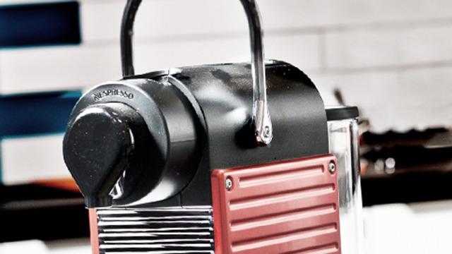 En moderne espressomaskine med sort og rød design, placeret på en køkkenbord.